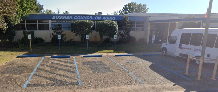 Exterior of Bossier Council on Aging building with parking lot. A white bus is parked in the lot.