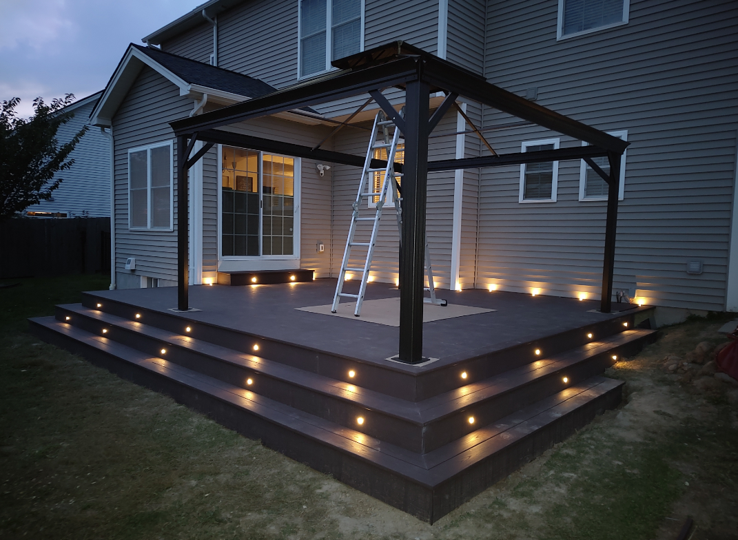 A deck with stairs and a pergola is lit up at night.