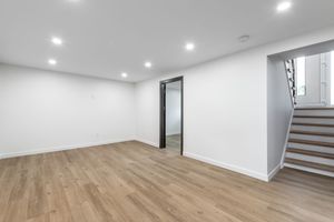 An empty basement with hardwood floors and white walls.