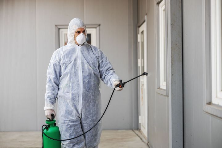 A man in a protective suit is spraying a wall with a sprayer.