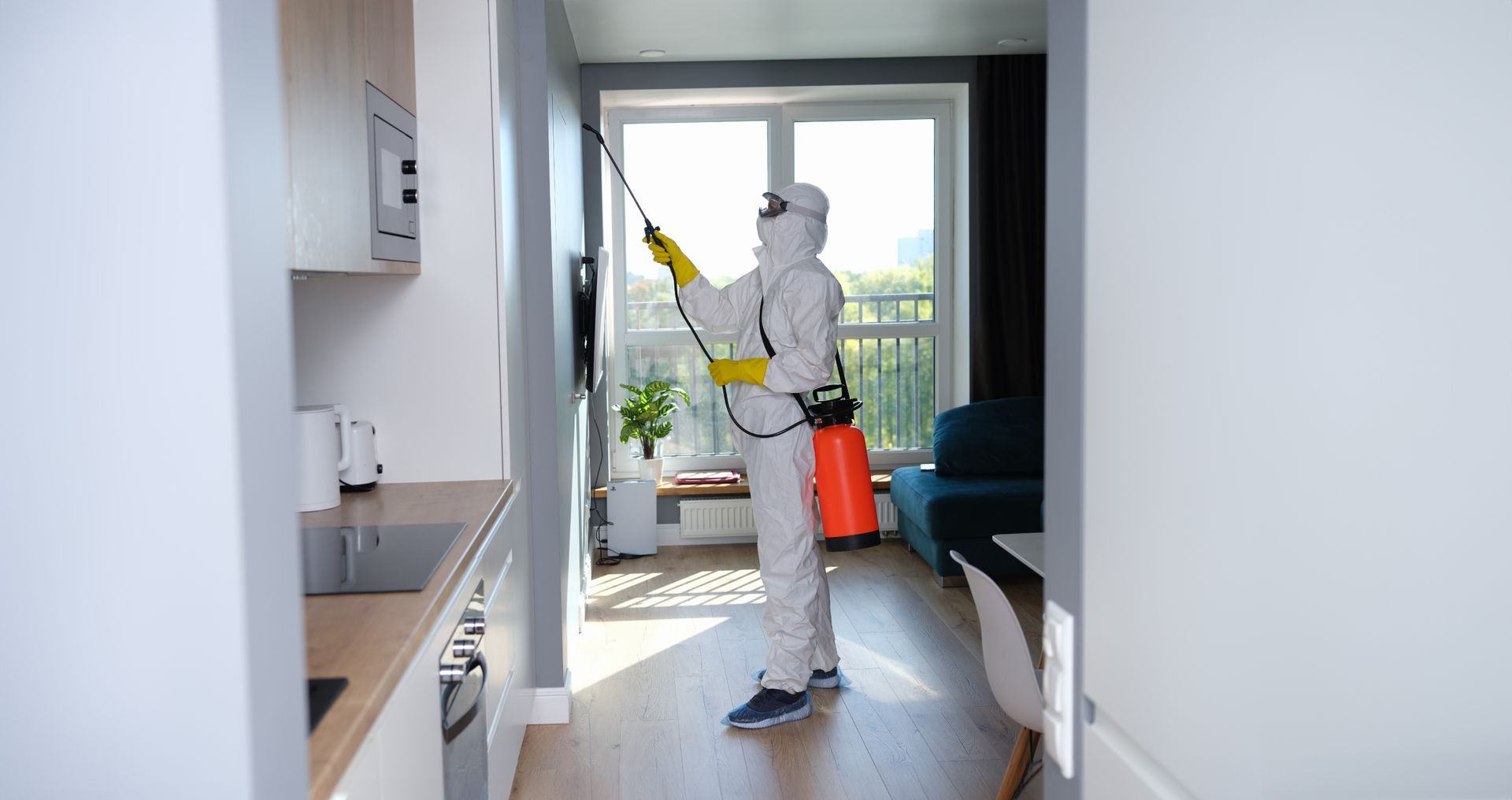 A man in a protective suit is spraying a drawer in a kitchen.