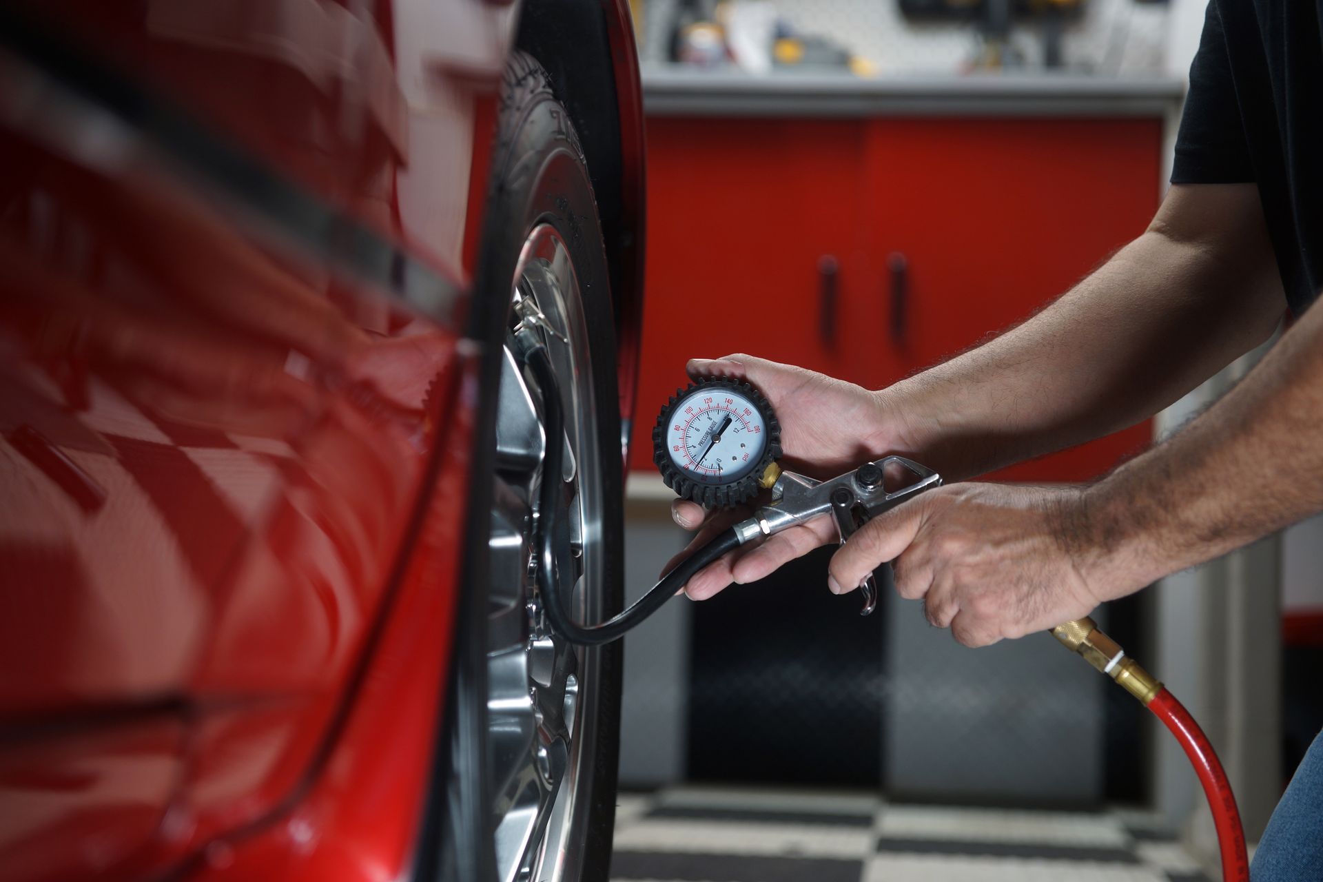 A man is checking the tire pressure of a red car.