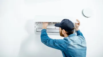 A man is installing an air conditioner on a wall.