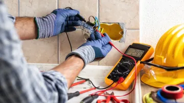 An electrician is working on an electrical outlet with a multimeter.