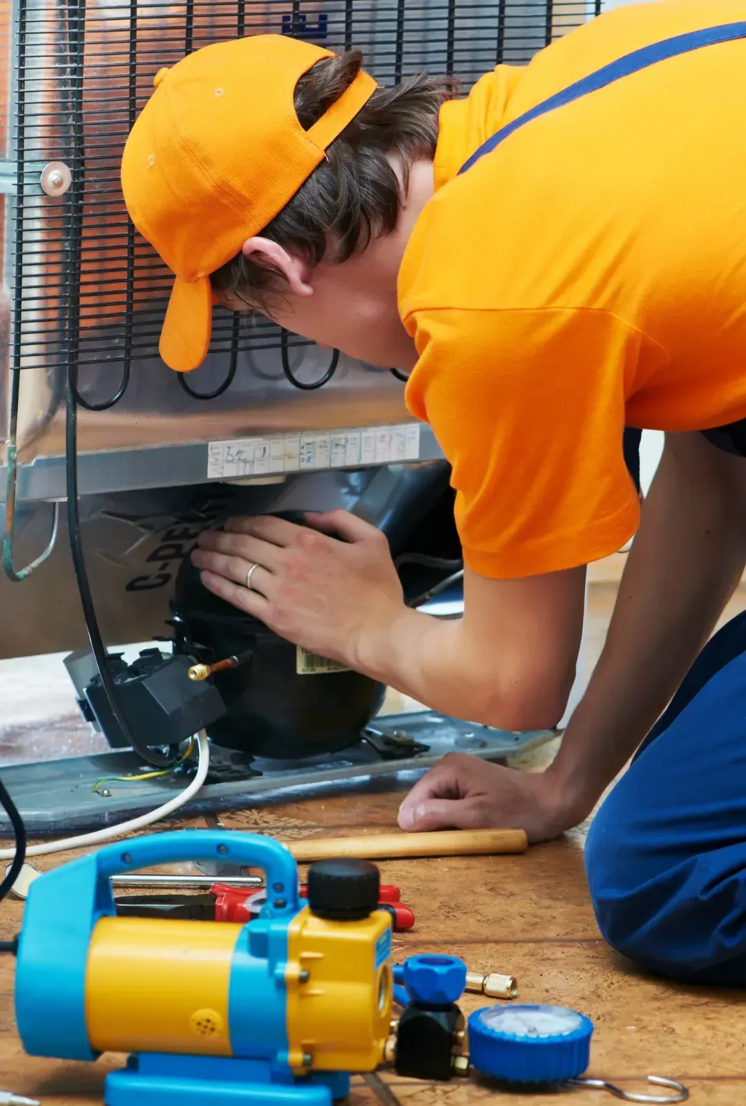 A man in an orange shirt is working on a refrigerator.