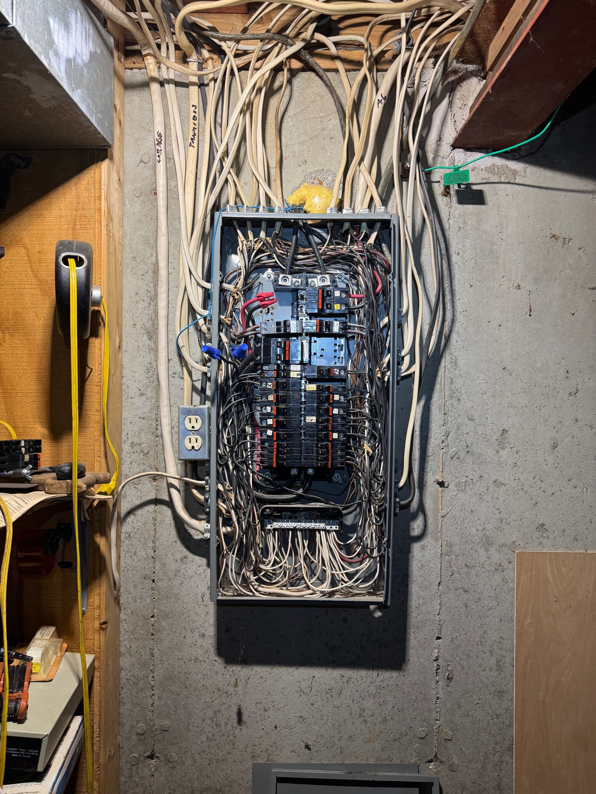 A very messy electrical box is hanging on a wall.