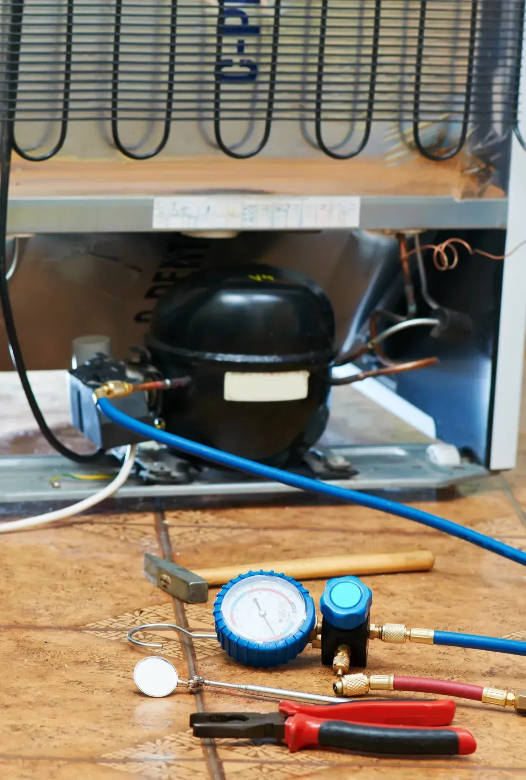 A refrigerator is being repaired with tools on the floor.