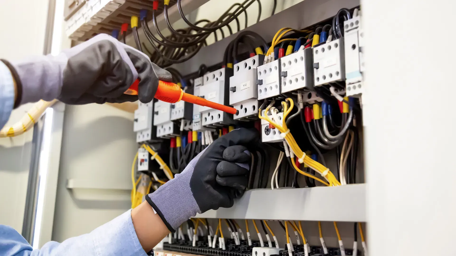 An electrician is working on an electrical box with a screwdriver.