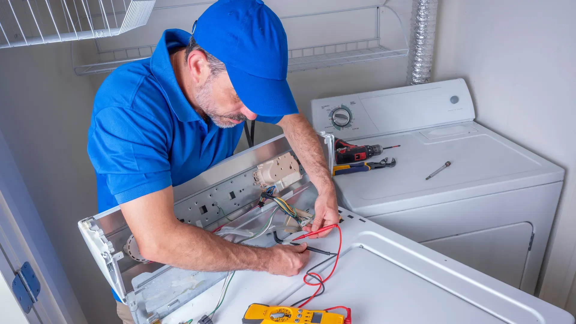 A man is fixing a washer and dryer in a laundry room.
