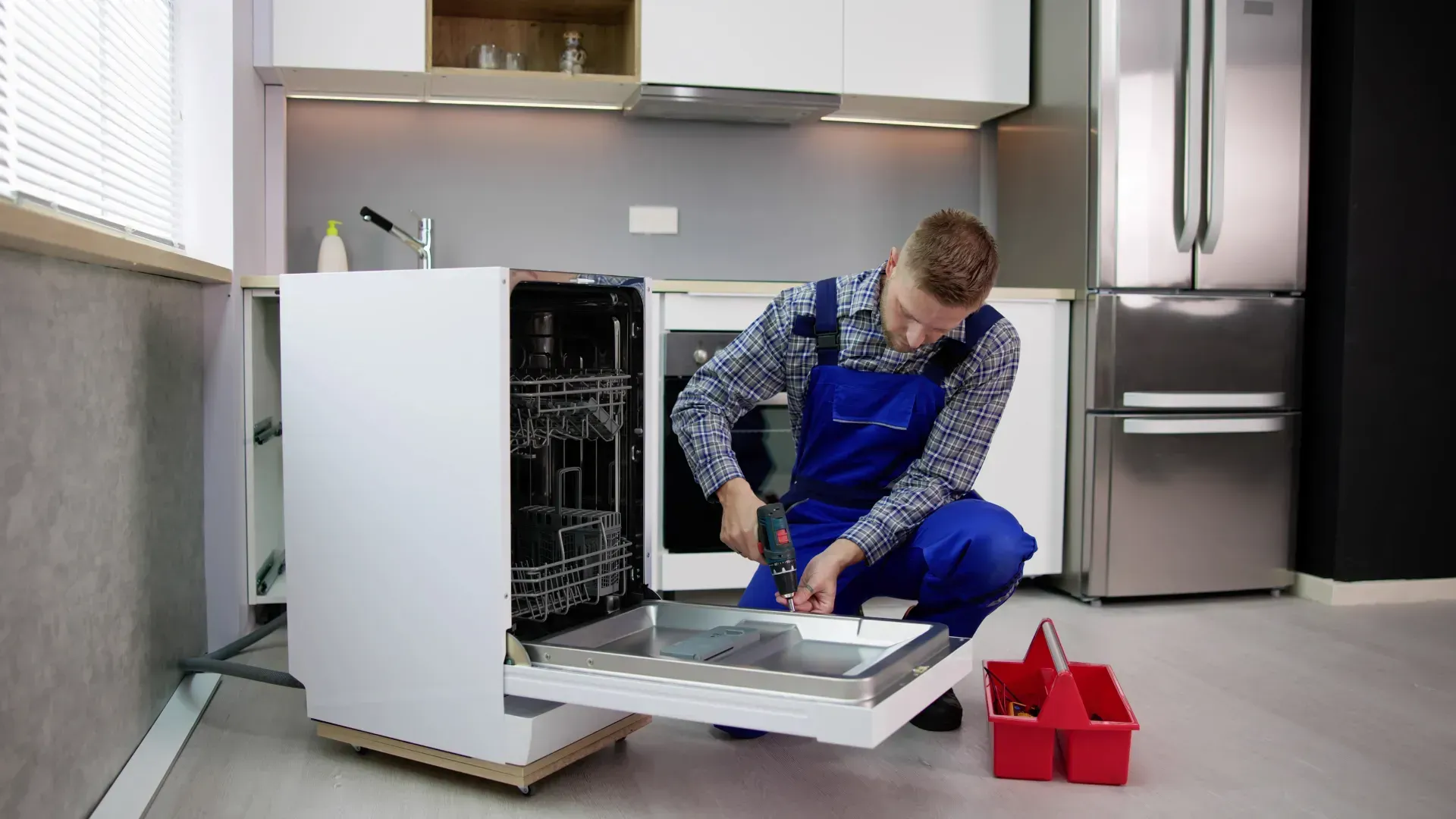 A man is fixing a dishwasher in a kitchen.