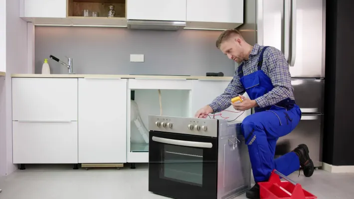 A man is fixing an oven in a kitchen.