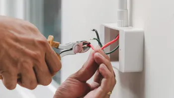 A person is working on an electrical box on a wall.