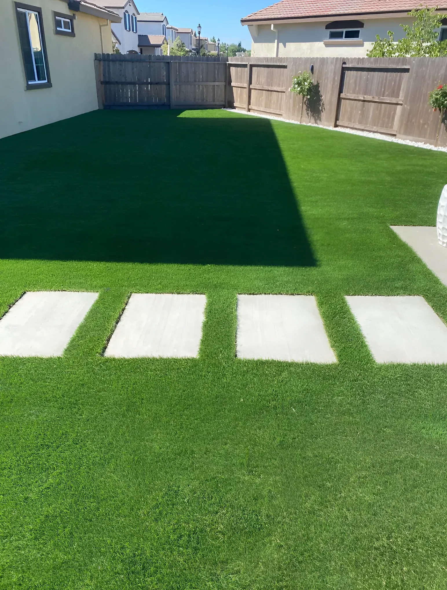 Backyard with green artificial turf and stone stepping stones. Wooden fences surround the area.