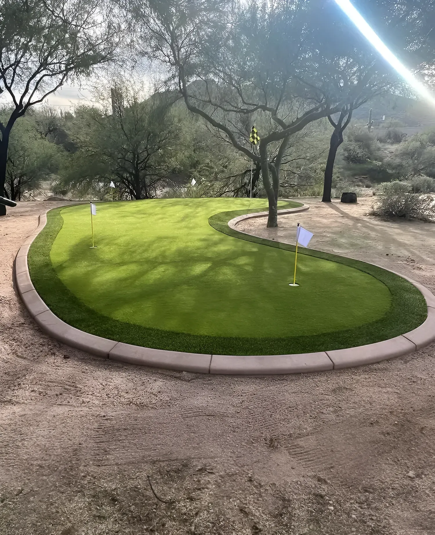 A well-manicured green with two flagsticks on a golf course, surrounded by light-colored gravel.