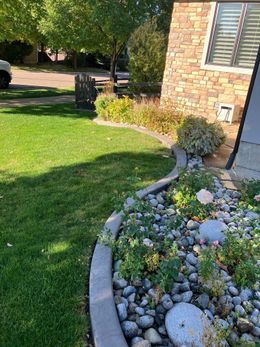 Lawn and garden bed along house with brick veneer and window, bordering a street.