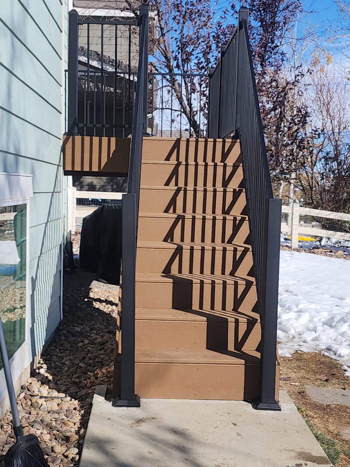 Outdoor stairs with brown steps and black railing, leading to a small deck.