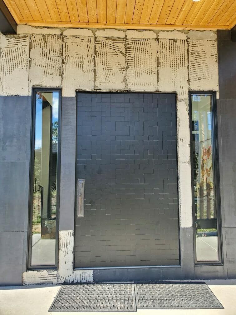 Black front door with sidelight windows, gray exterior, and wood ceiling.