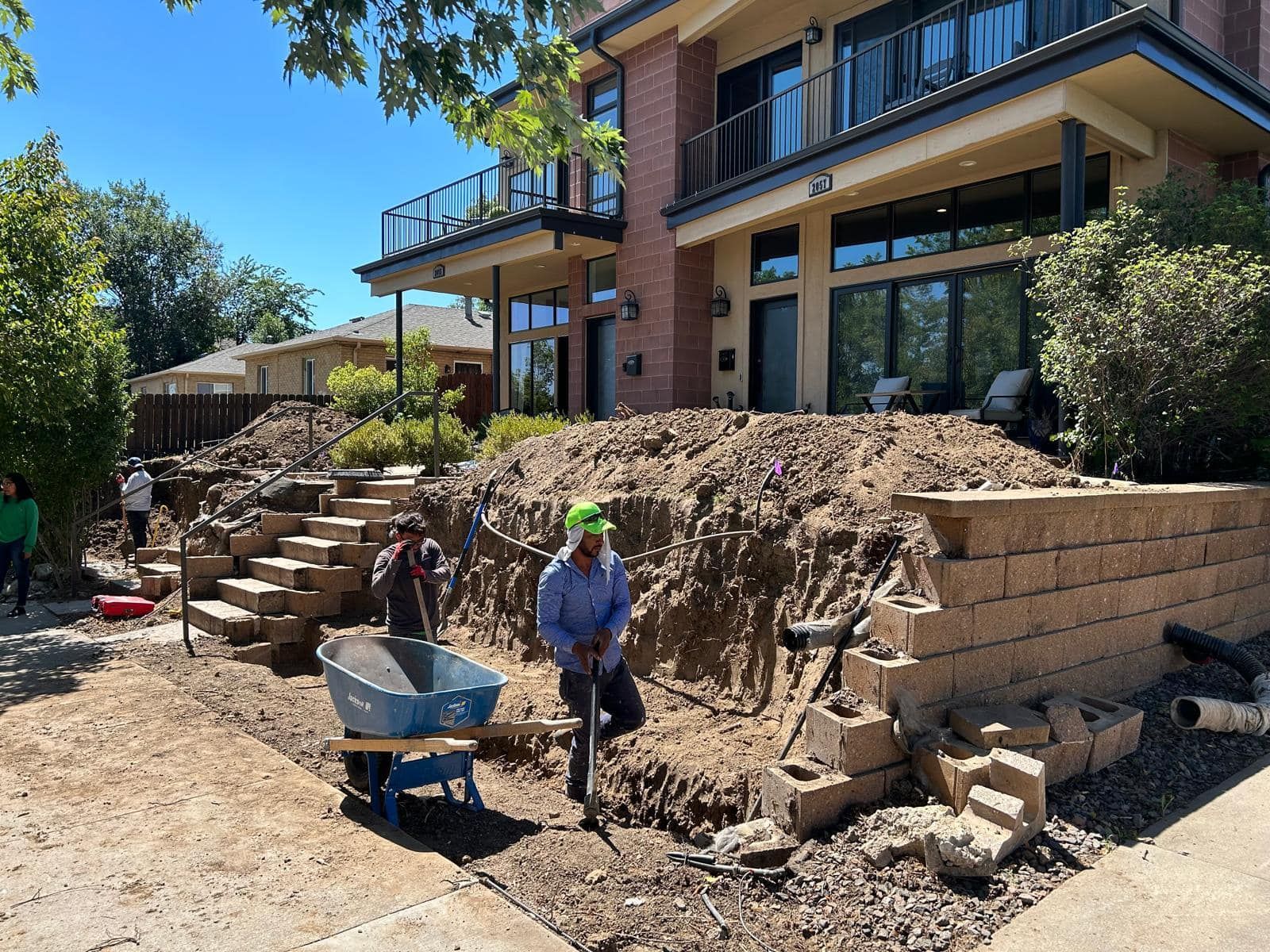 Construction workers building retaining wall and steps in front of a house.