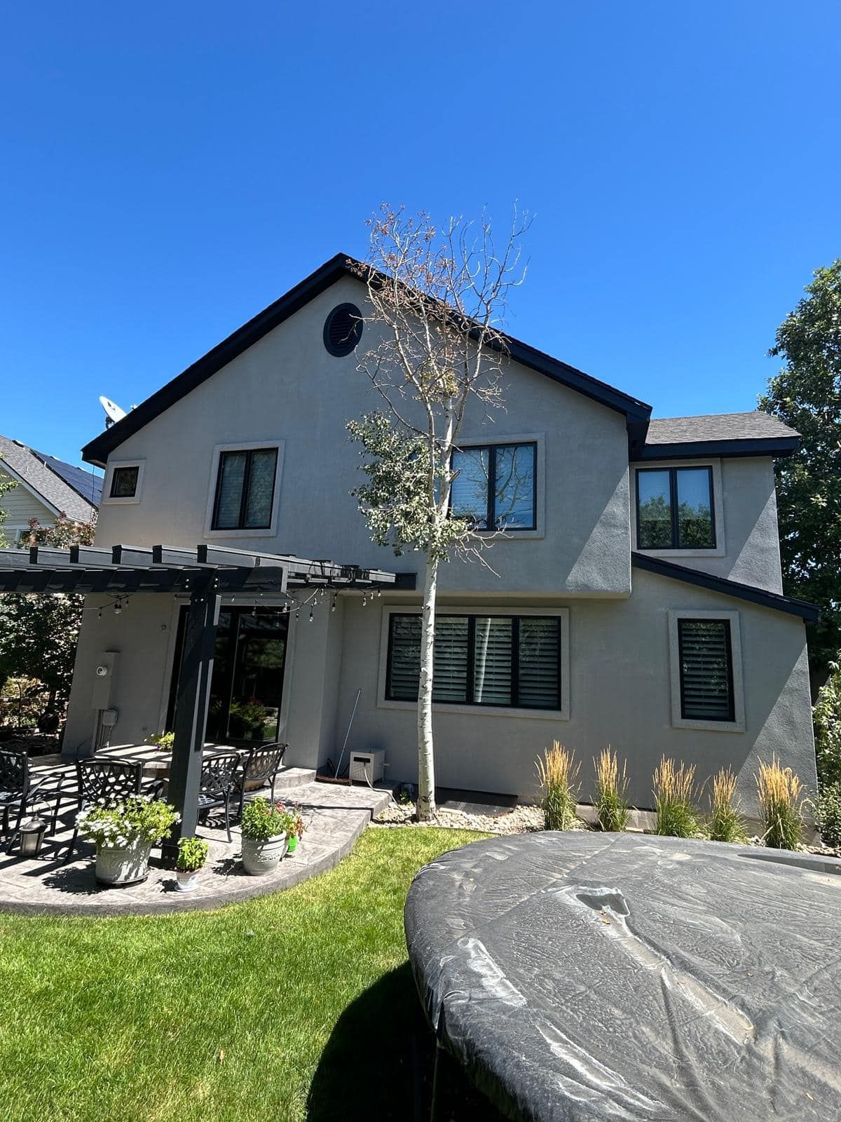 Rear view of a two-story stucco house with a black roof and trim, next to a backyard and spa.