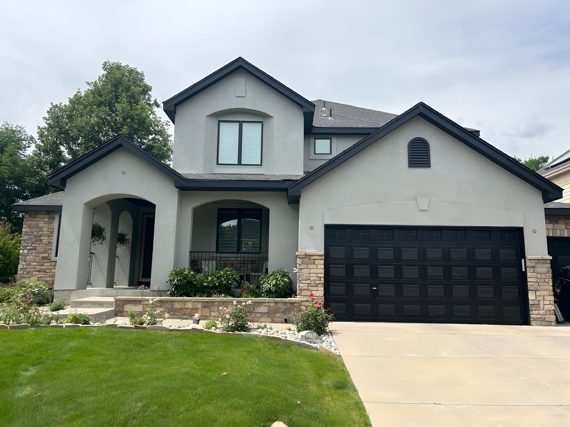 Two-story stucco house with a black garage door and trim, stone accents, and a green lawn.