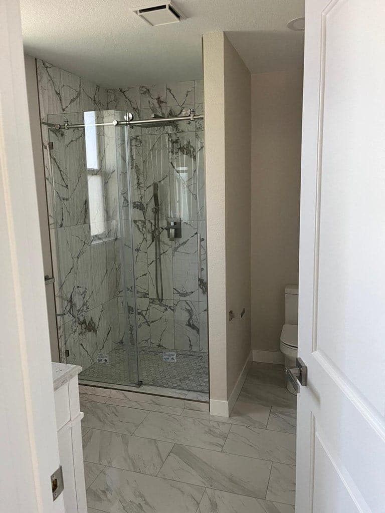 Bathroom with marble-look tile, glass shower enclosure, and white door.