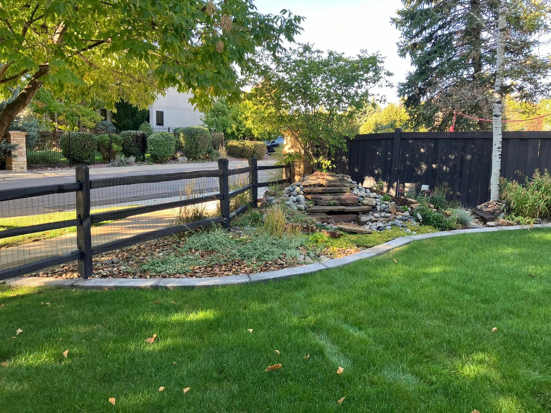 Lush green lawn with a black fence, rock steps, and landscaping.