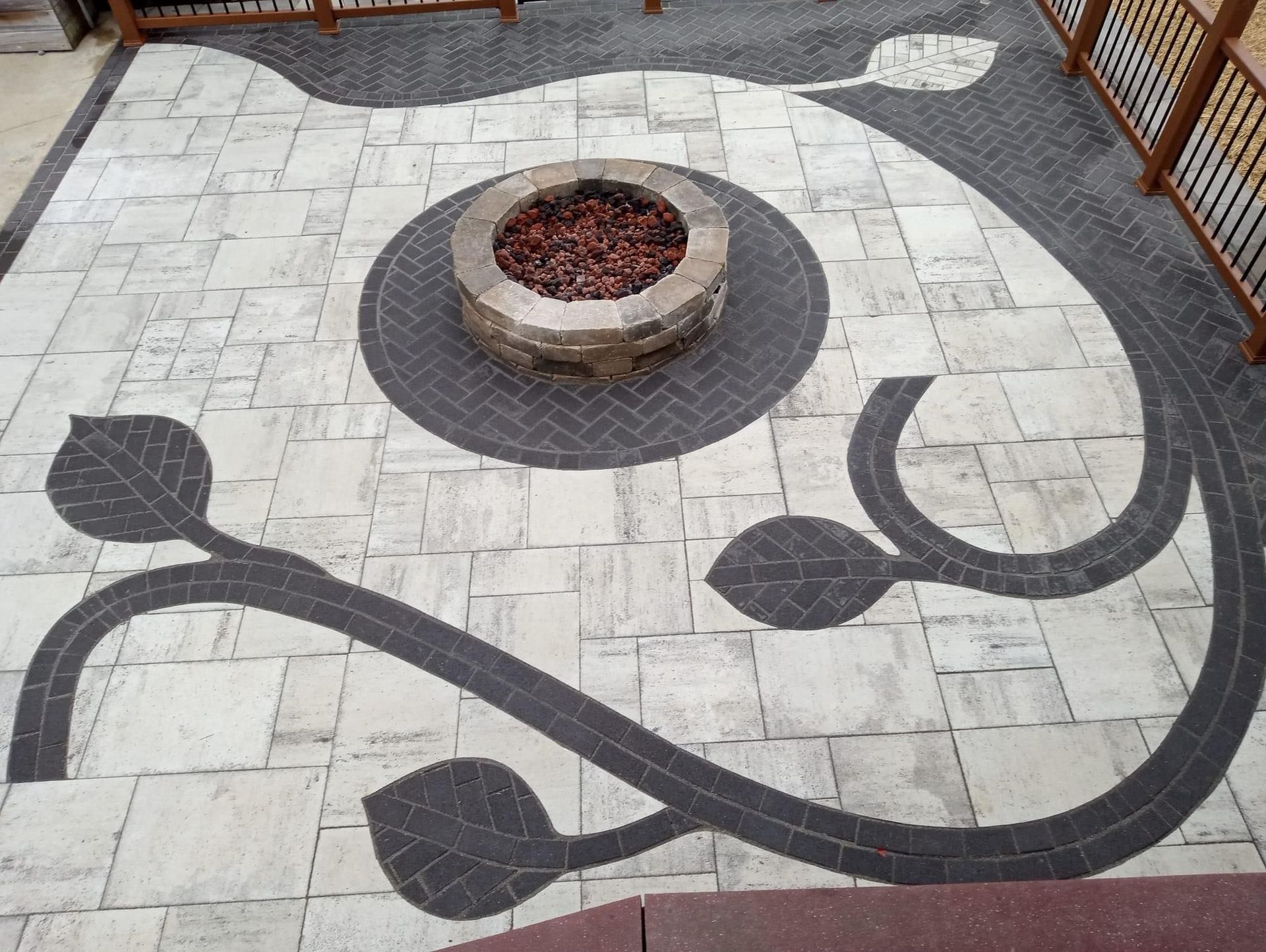 Patio with fire pit, stone paving with dark curving vine design and leaf details.