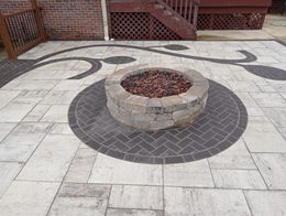 Brick patio with a fire pit surrounded by dark brickwork and decorative patterns.