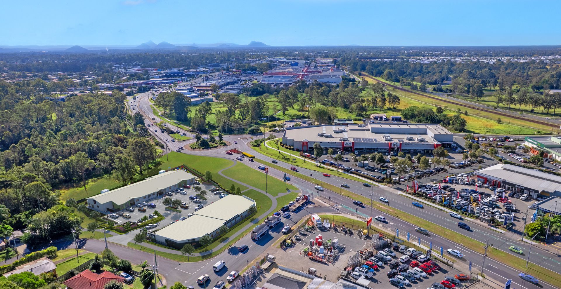 Aerial view of commercial buildings, roads, parking, and green space under a blue sky.