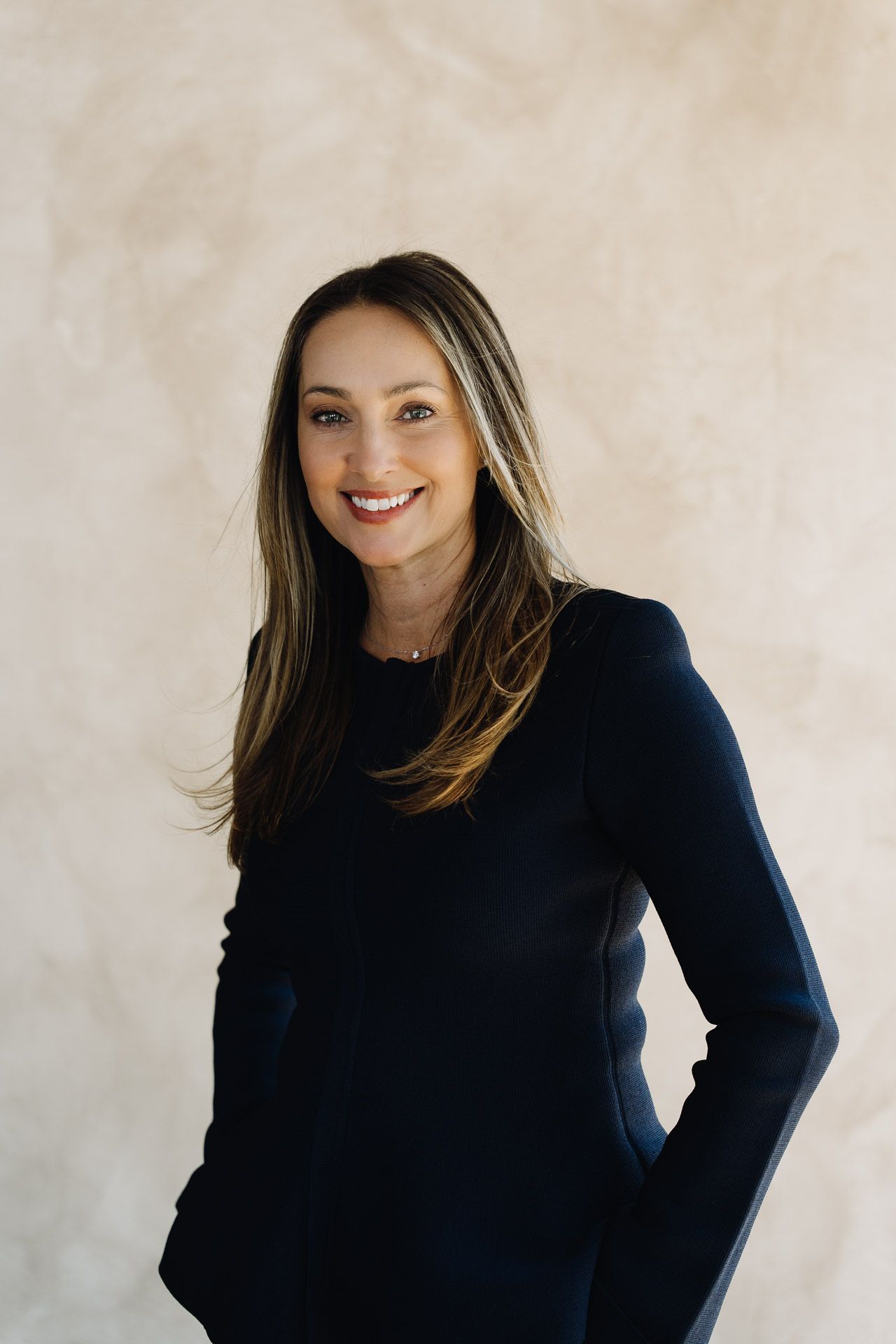 Man in a dark blazer, white shirt, and striped tie smiles. Pale background.