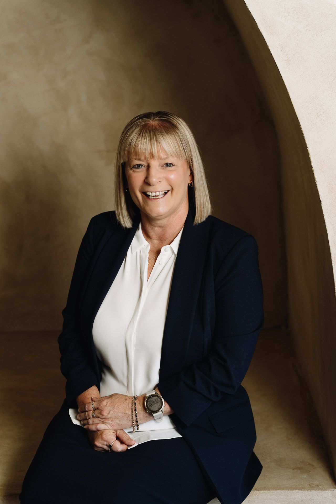 Woman in business attire smiles, sitting under an archway.