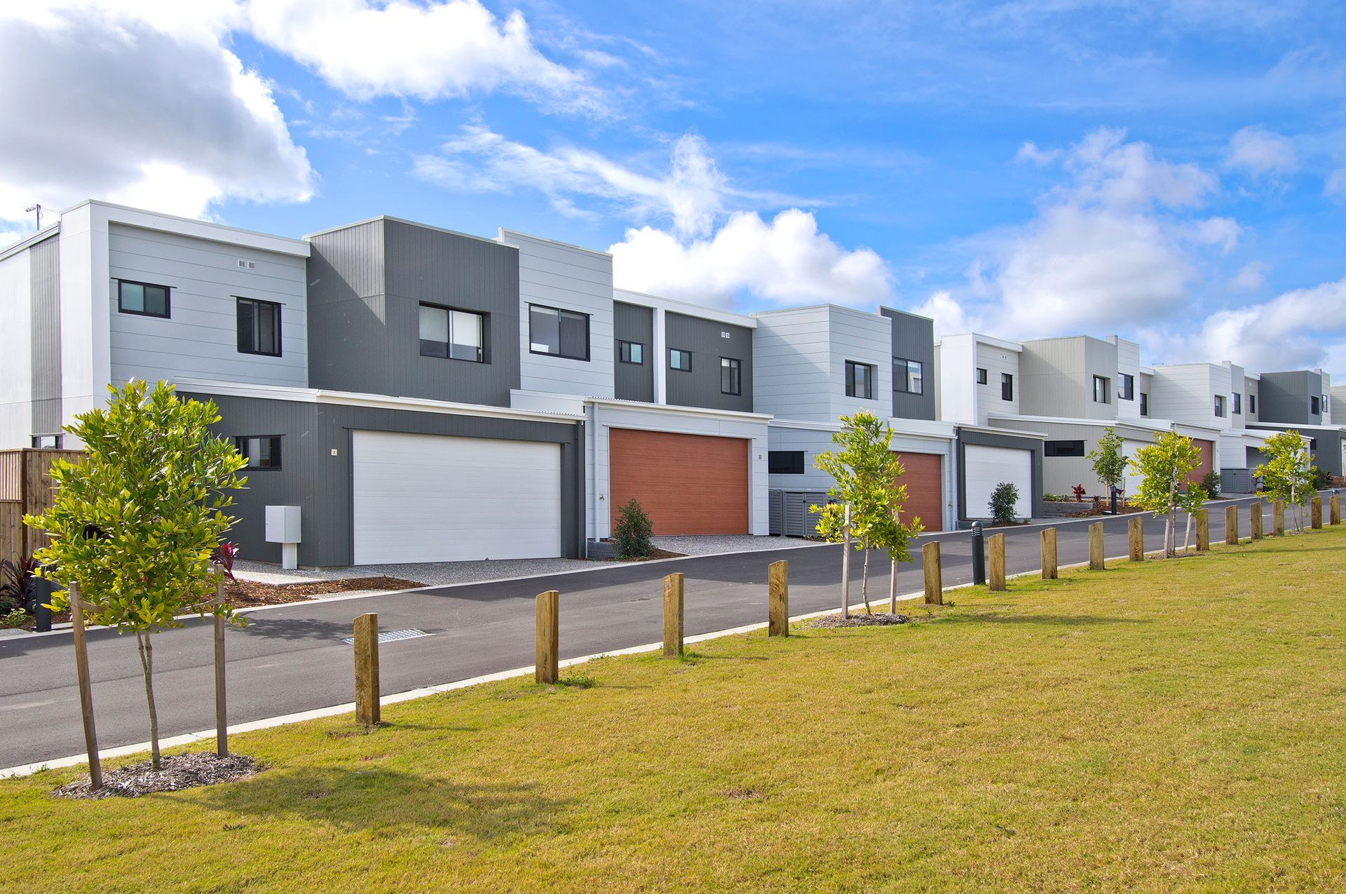 Row of modern townhouses with white, gray, and brown exteriors and garages, under a blue sky.