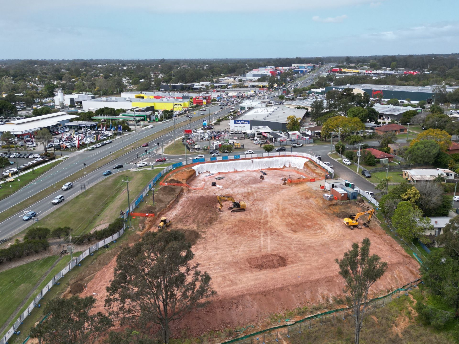 Aerial view of a construction site with earthmovers. Highway and commercial buildings in the background.