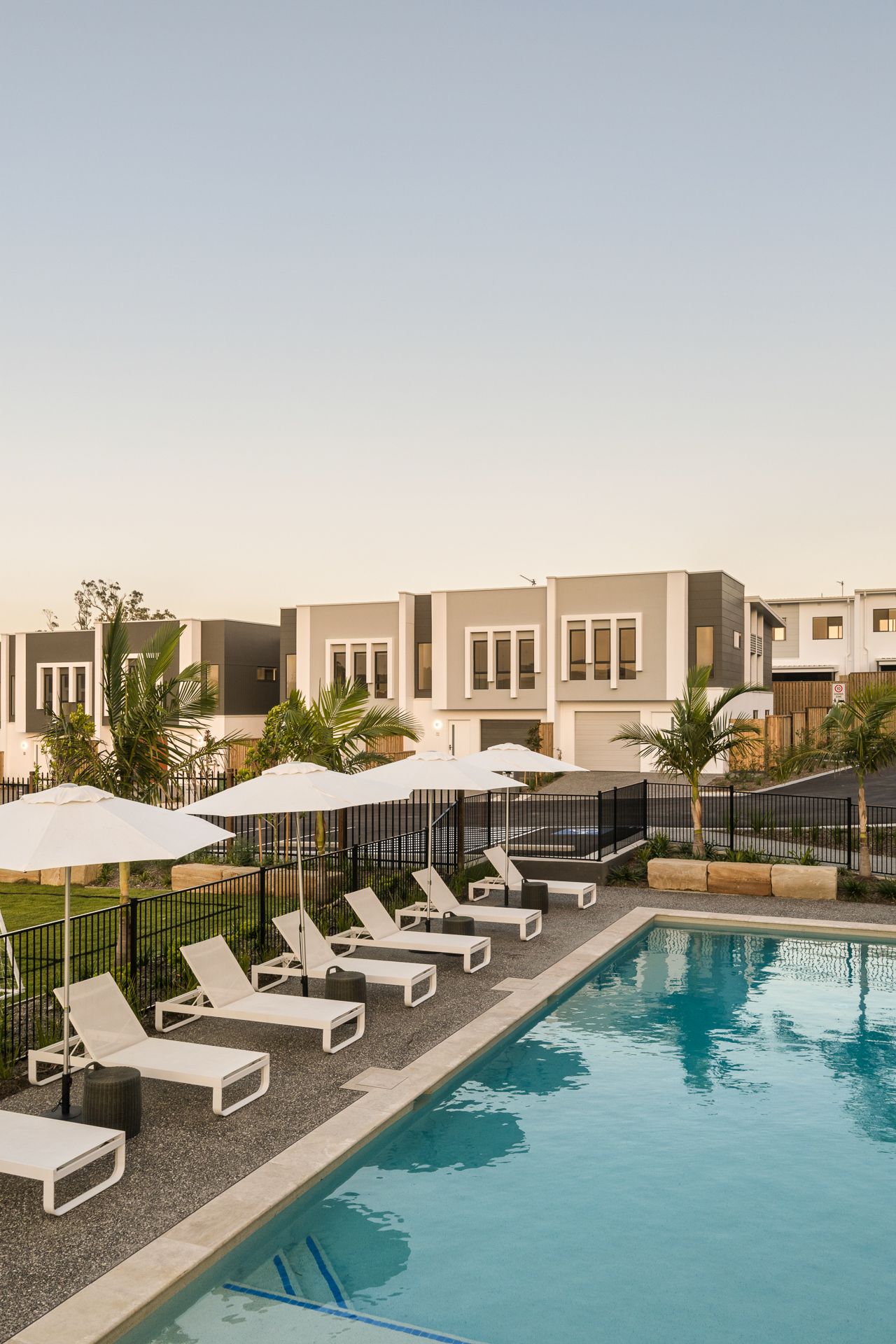 Poolside lounge chairs, umbrellas, and a swimming pool in front of modern townhouses.
