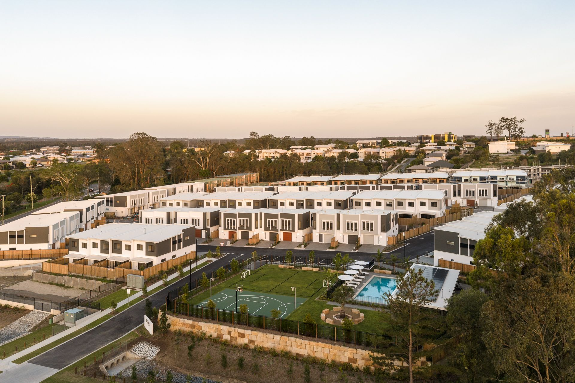 Aerial view of a modern townhome complex with a pool, sports court, and green spaces.