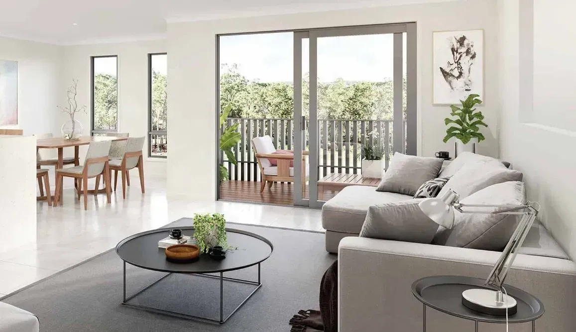 Modern living room with balcony access. White walls, grey sofa, round coffee table, and dining table visible.