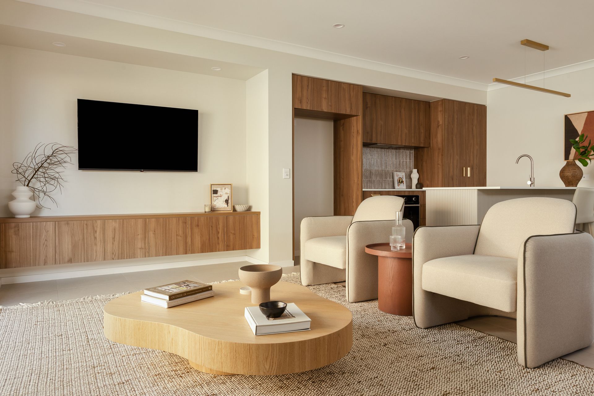 Living room with wooden cabinets, beige armchairs, and a round coffee table on a shaggy rug.