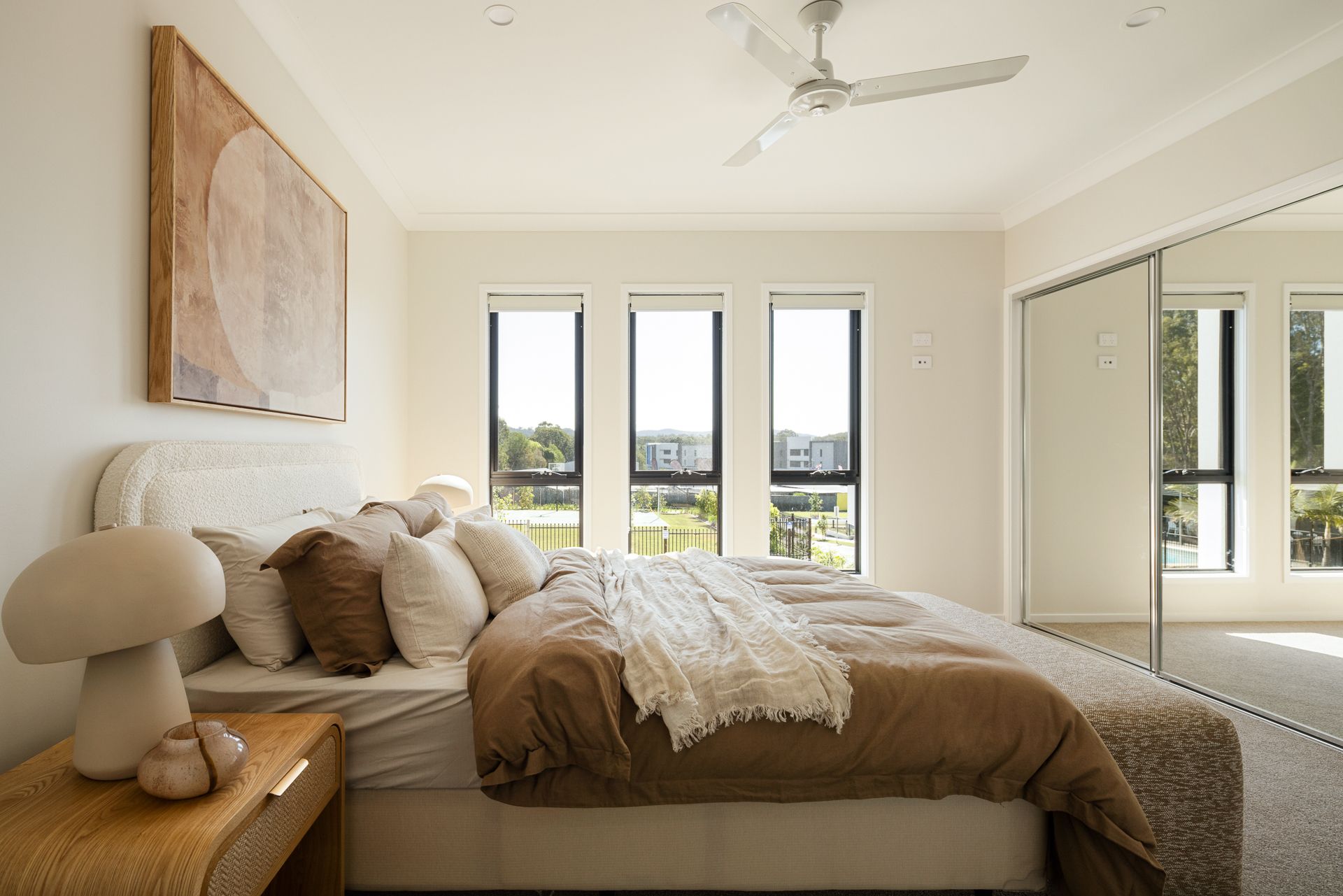 Bedroom with large bed, neutral tones, windows, artwork, and side table with mushroom decor.
