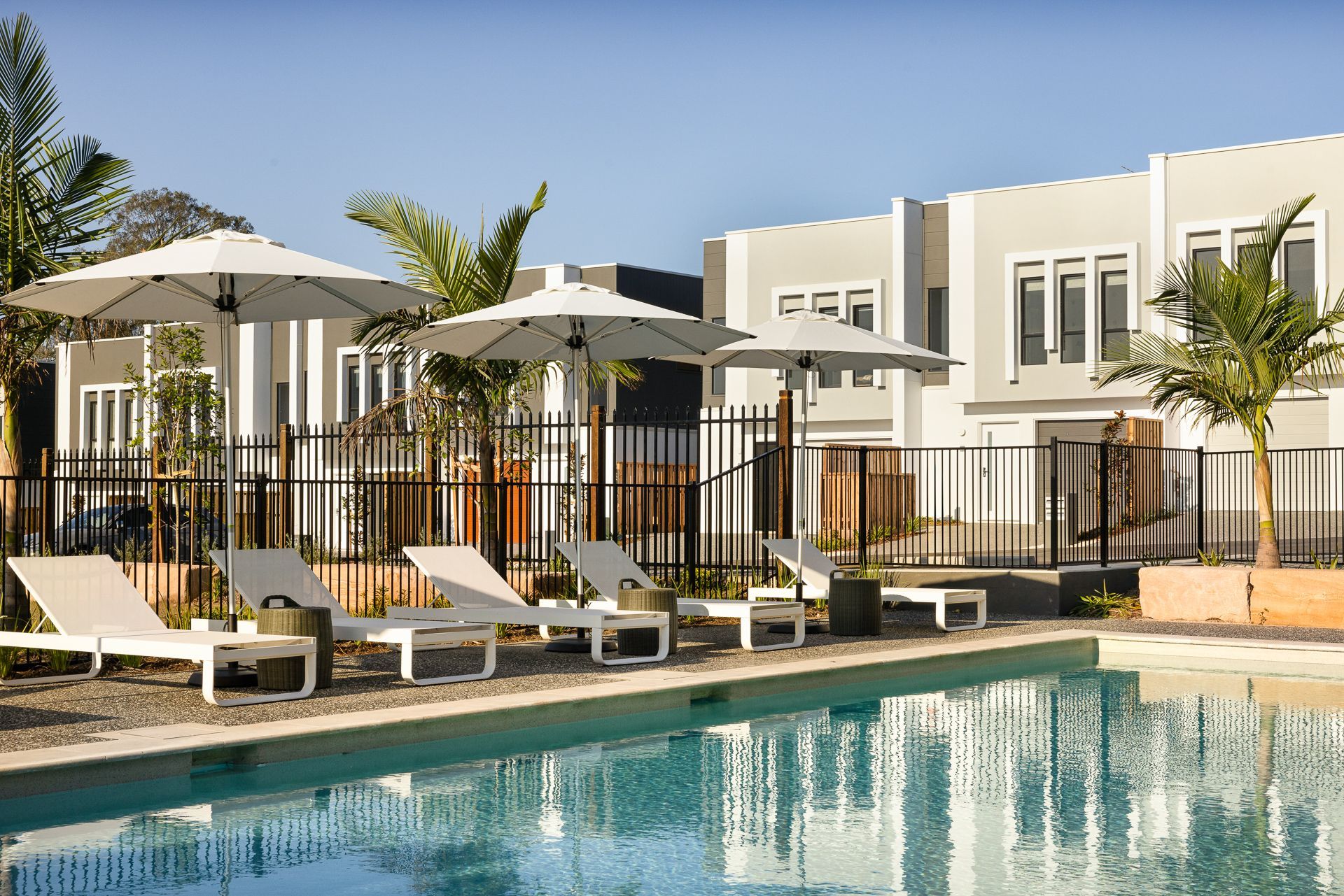 Poolside scene with lounge chairs, umbrellas, and modern buildings.
