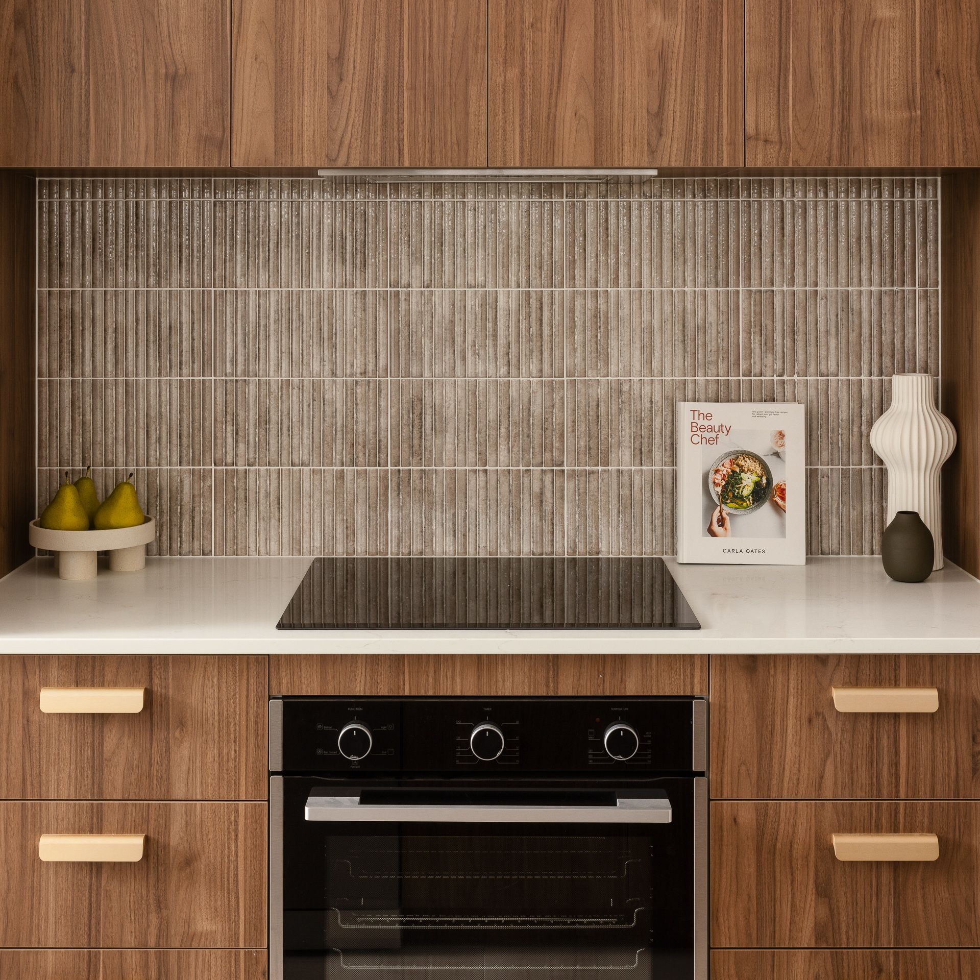 Kitchen with wood cabinets, white countertop, and gray backsplash with cookbook and pear decoration.