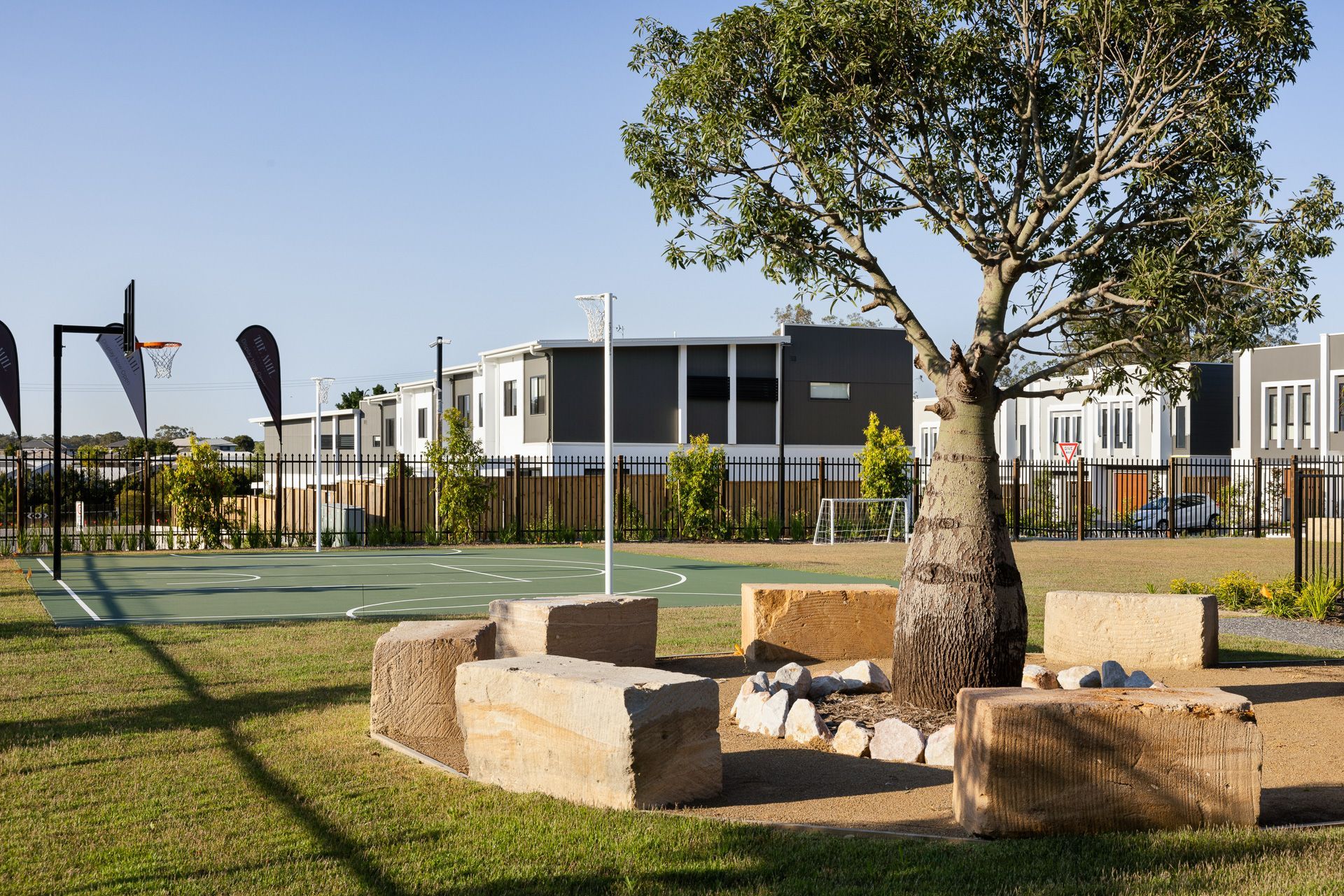Playground with a basketball hoop, fire pit, and tree in front of houses.