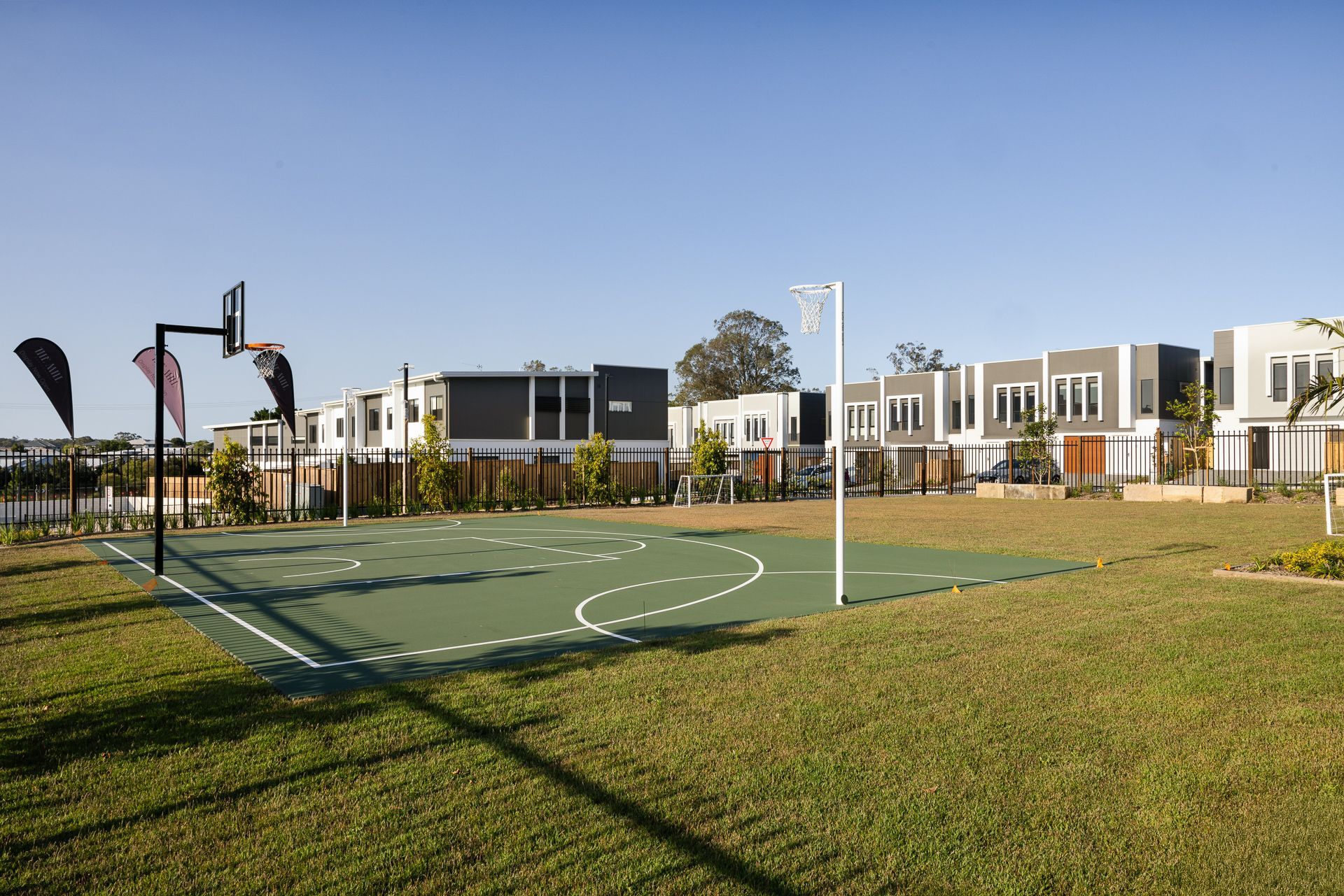 Basketball and netball court in a green space, with modern townhouses in the background.