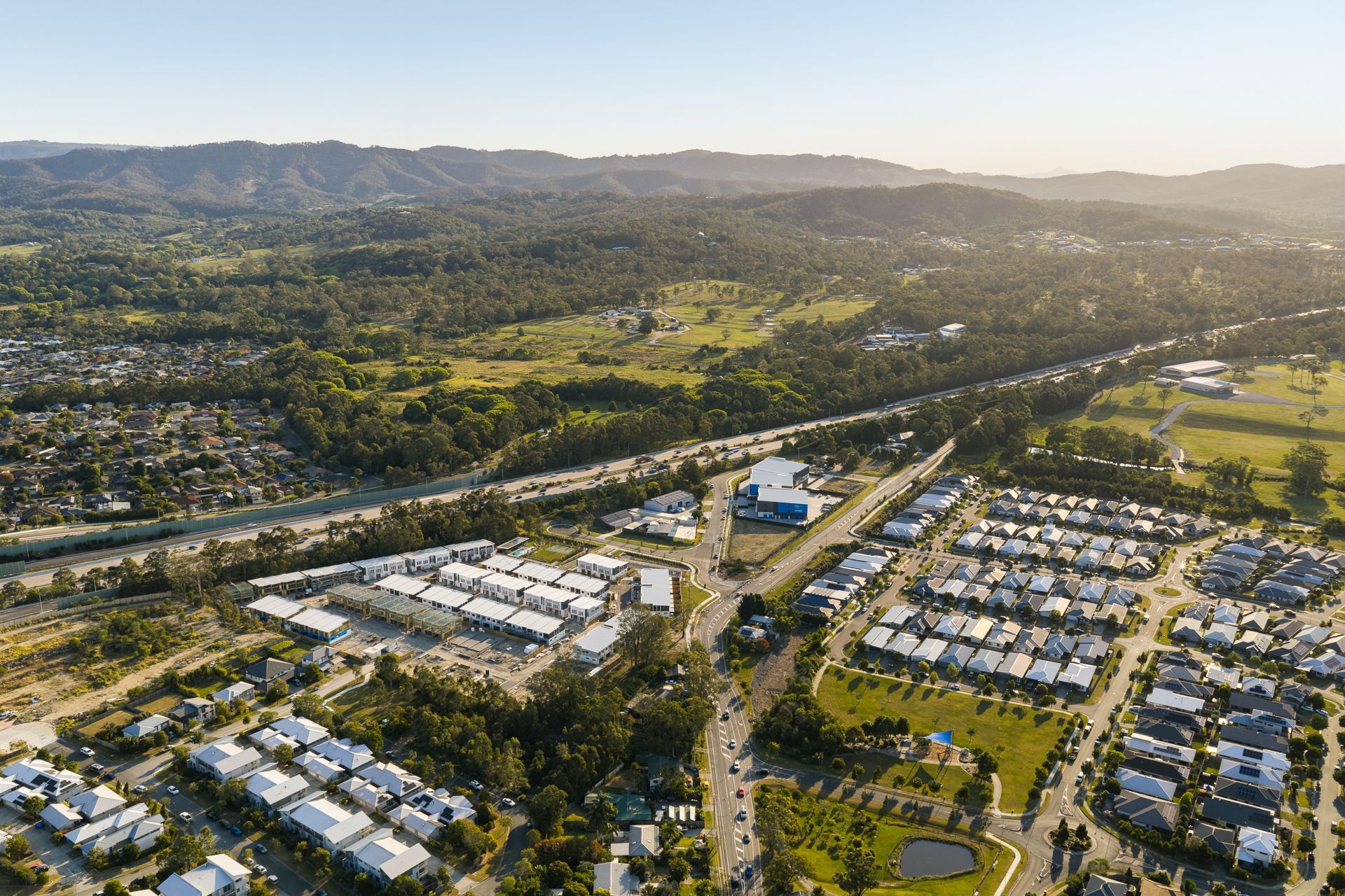Aerial view of a suburban neighborhood with roads, buildings, and green landscape leading to distant hills.