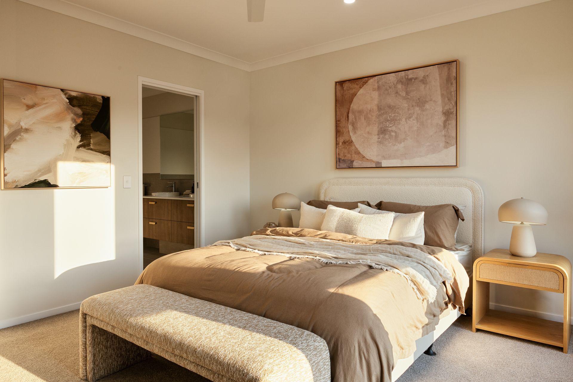 Sunlit beige bedroom with a bed, nightstand, wall art, and open doorway