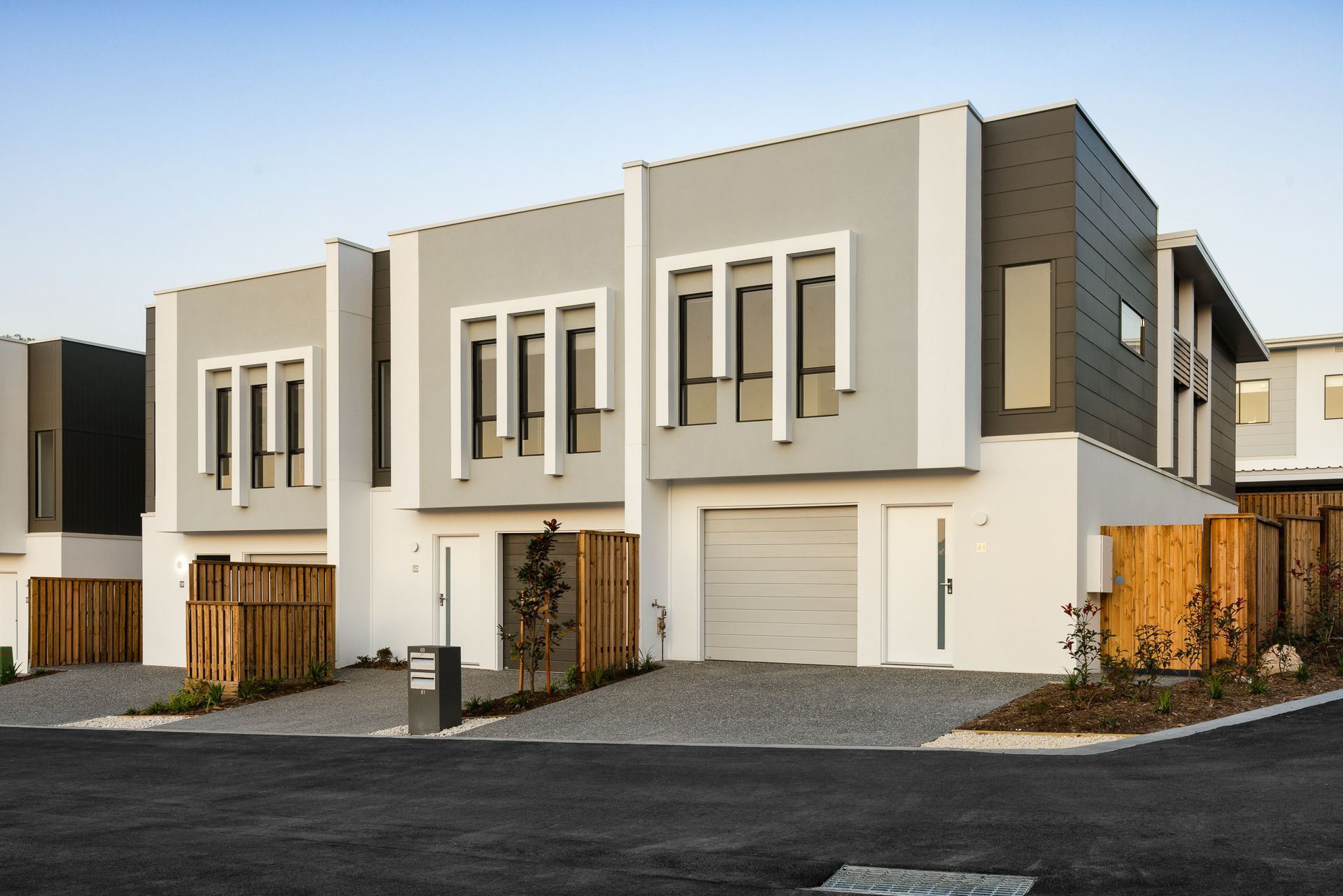 Modern townhouses with gray and white exteriors, driveway, and wooden fences.