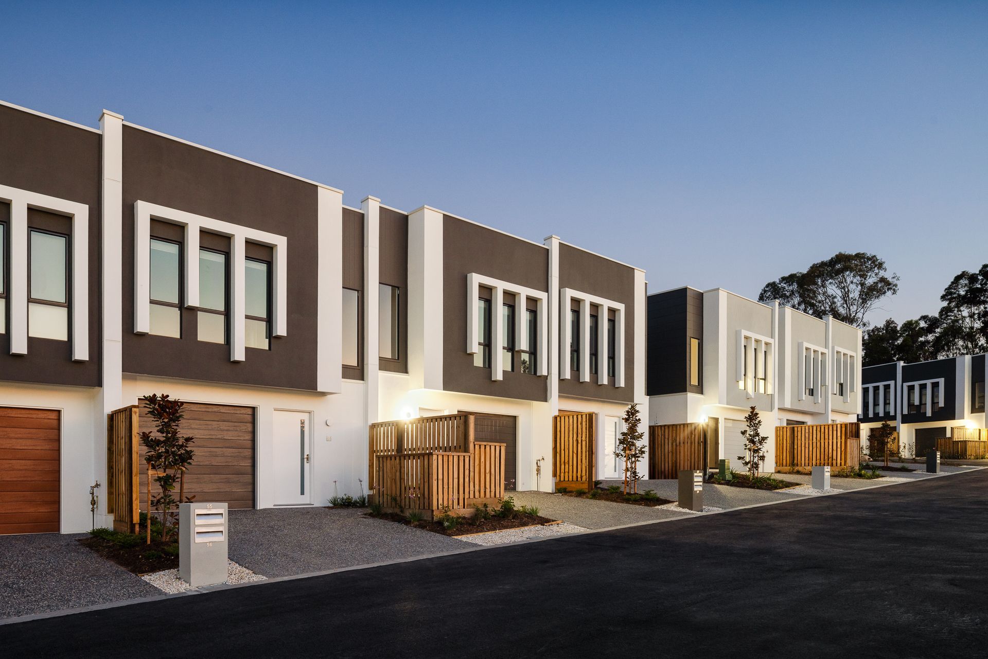 Row of modern townhouses with gray and white exteriors, wooden garage doors, and a blue sky.