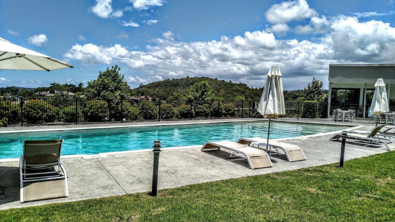 Swimming pool with lounge chairs, umbrellas, and a view of trees under a blue, cloudy sky.