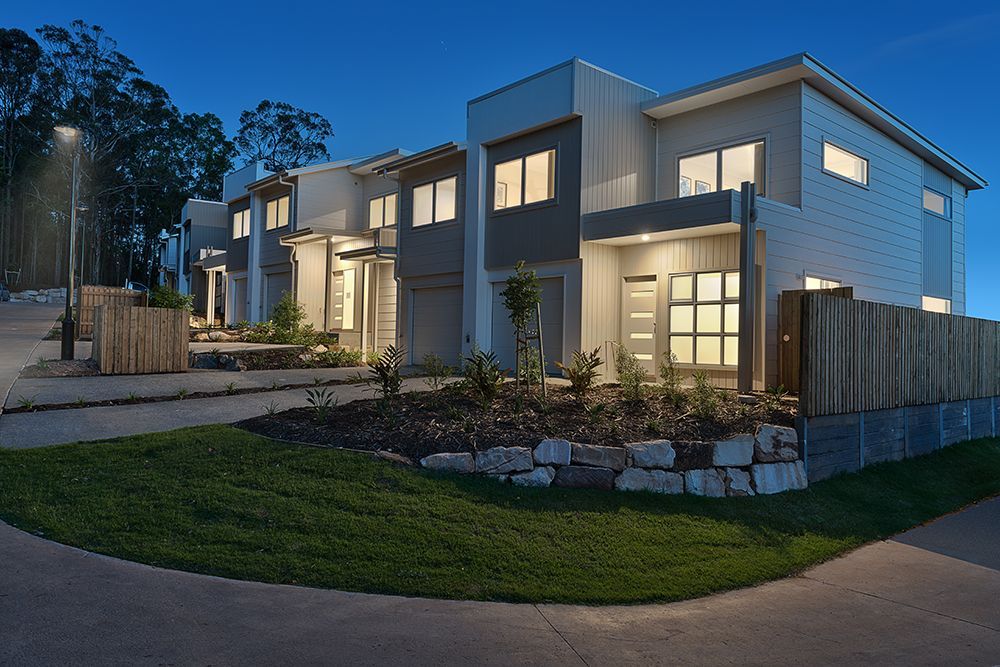 Row of modern townhouses at dusk with illuminated windows and landscaped yards.