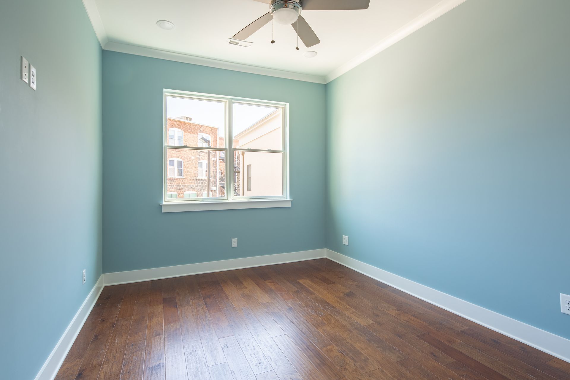 Empty room with blue walls, a window, hardwood floor, and a ceiling fan.