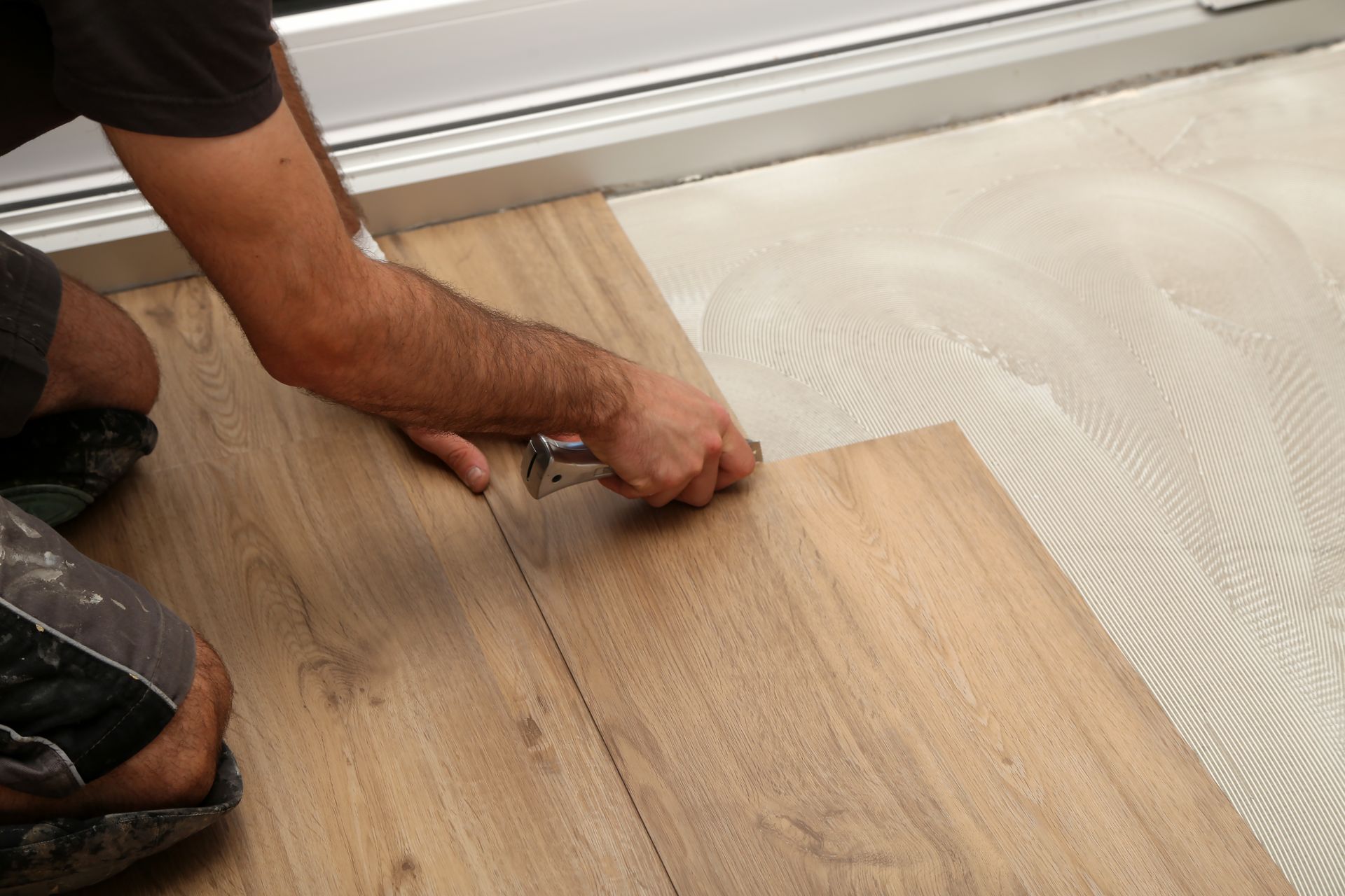 Person installing wooden floorboards, using a tool to connect them. Glue visible.
